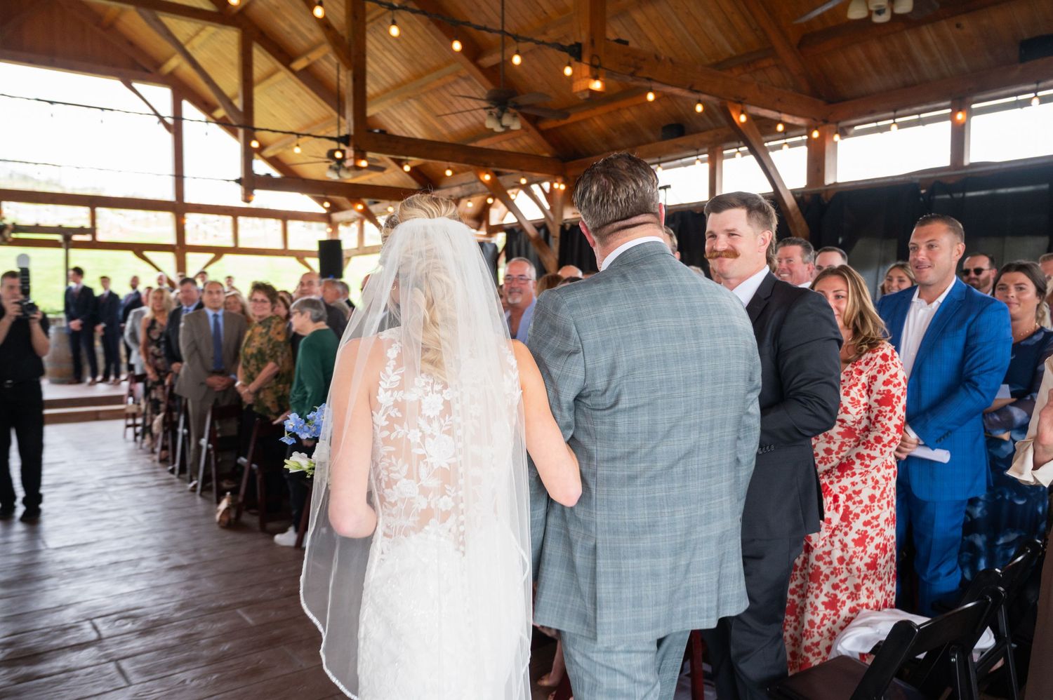 Father walking bride down the aisle at an outdoor covered wedding ceremony with seated guests.