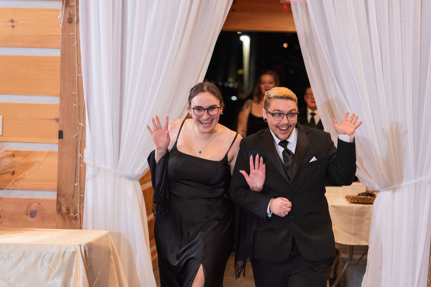 Excited couple makes grand entrance at wedding reception through draped white curtain doorway.