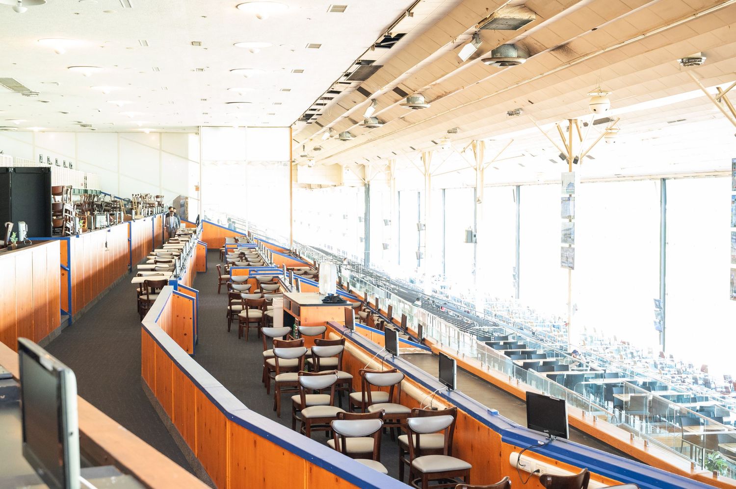 Empty stadium club level with wooden booths, blue accents, and floor-to-ceiling windows overlooking the field.