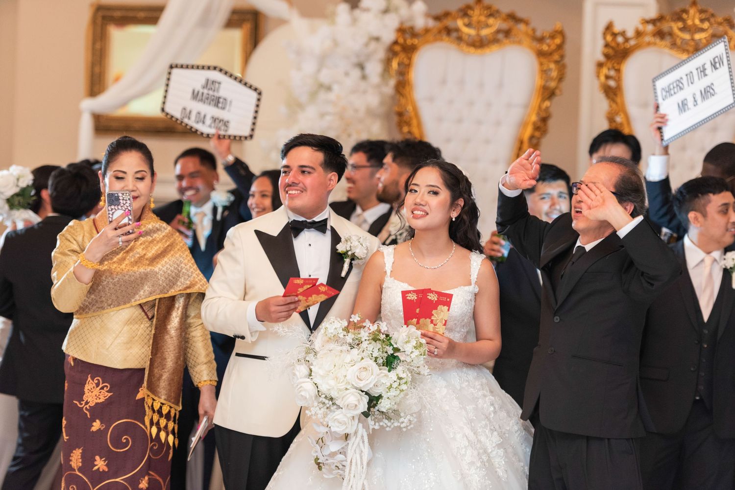 A joyful wedding ceremony with a bride in a white gown and groom in a tuxedo, surrounded by guests holding signs.
