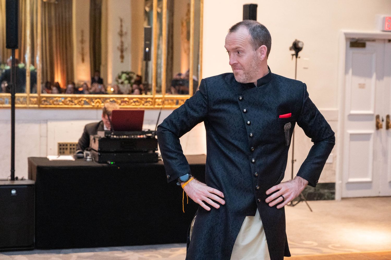Man in elegant dark kurta with hands on hips posing at an indoor event.