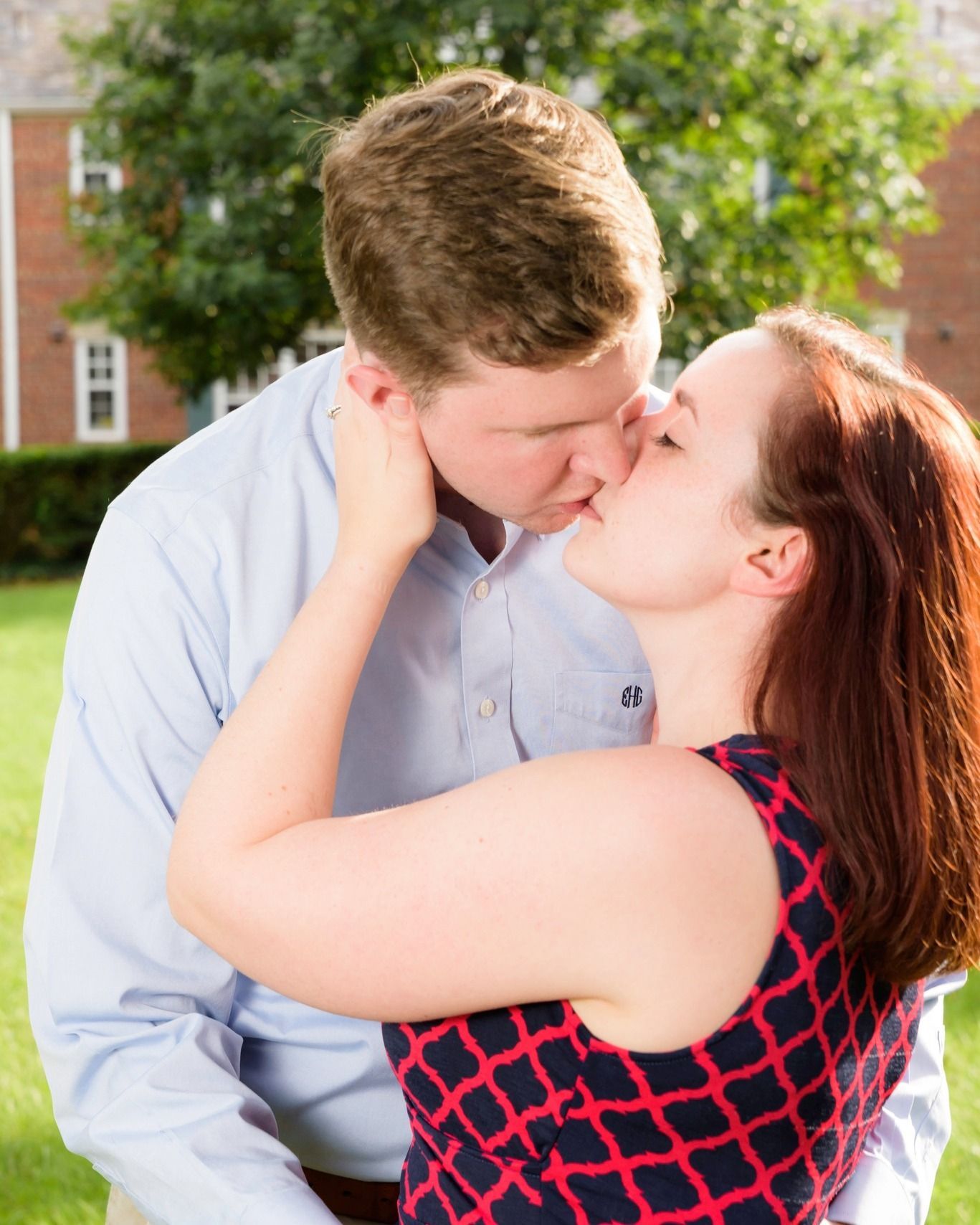 Couple sharing a romantic kiss outdoors on a sunny day near a brick building.