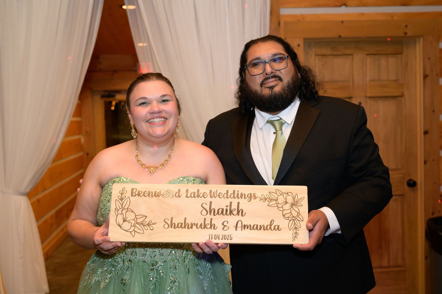 Newlyweds Shaikh and Amanda pose with a wooden wedding sign at Beechwood Lake Weddings venue.