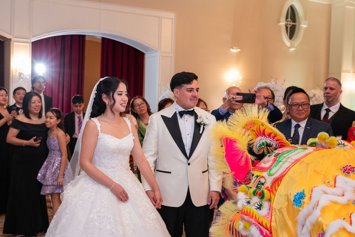 Bride and groom walk past colorful lion dance performers at traditional Chinese wedding reception ceremony.