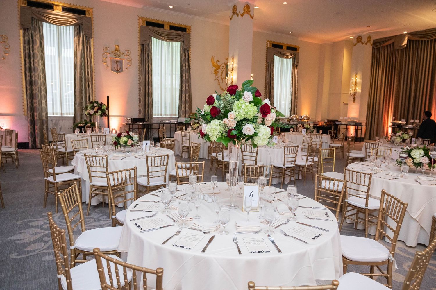 Elegant wedding reception ballroom with round tables, gold chiavari chairs, and floral centerpieces.