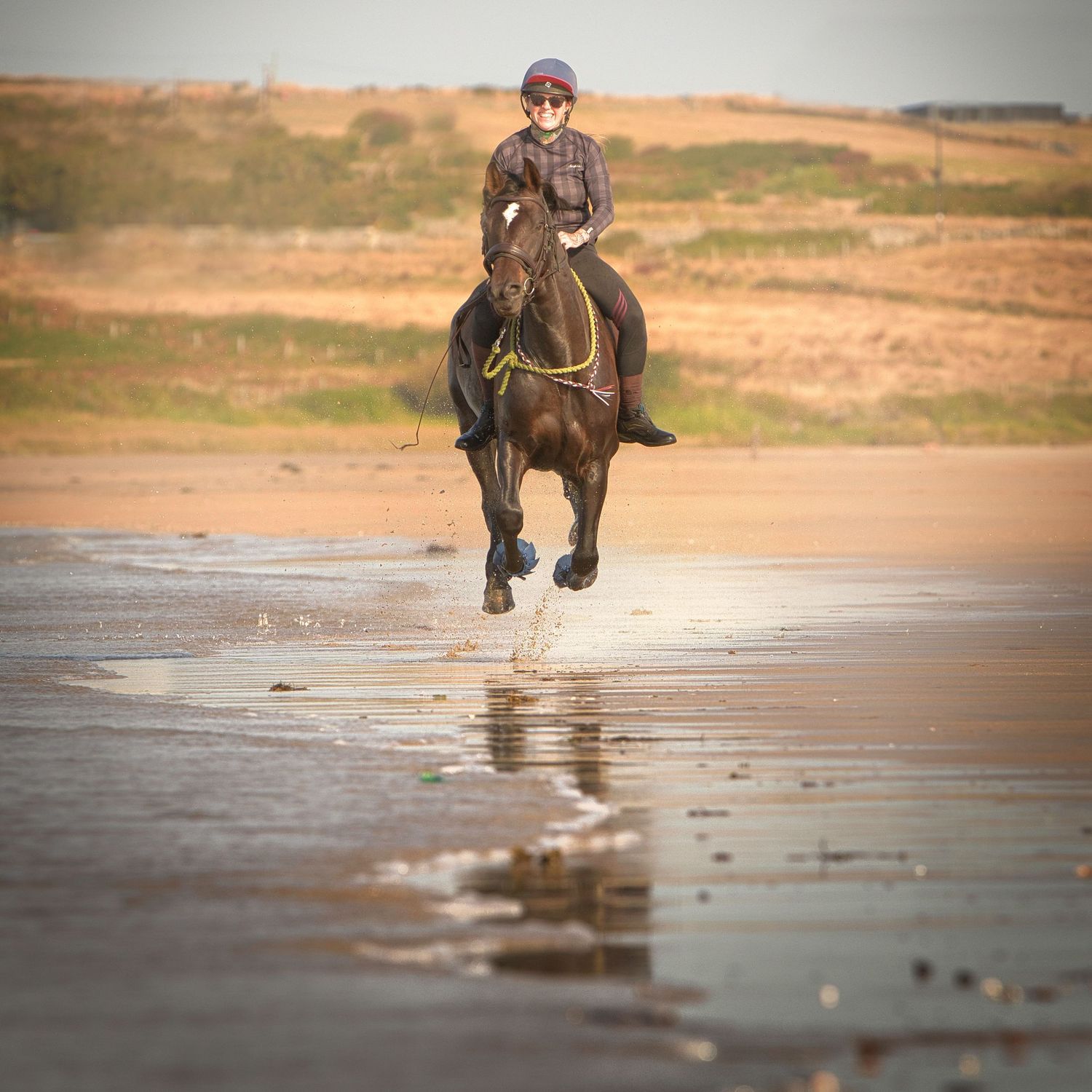 Galloping horse splashing through waves on the beach, rider smiling with joy during an equine photography shoot. Aberffraw, North Wales,