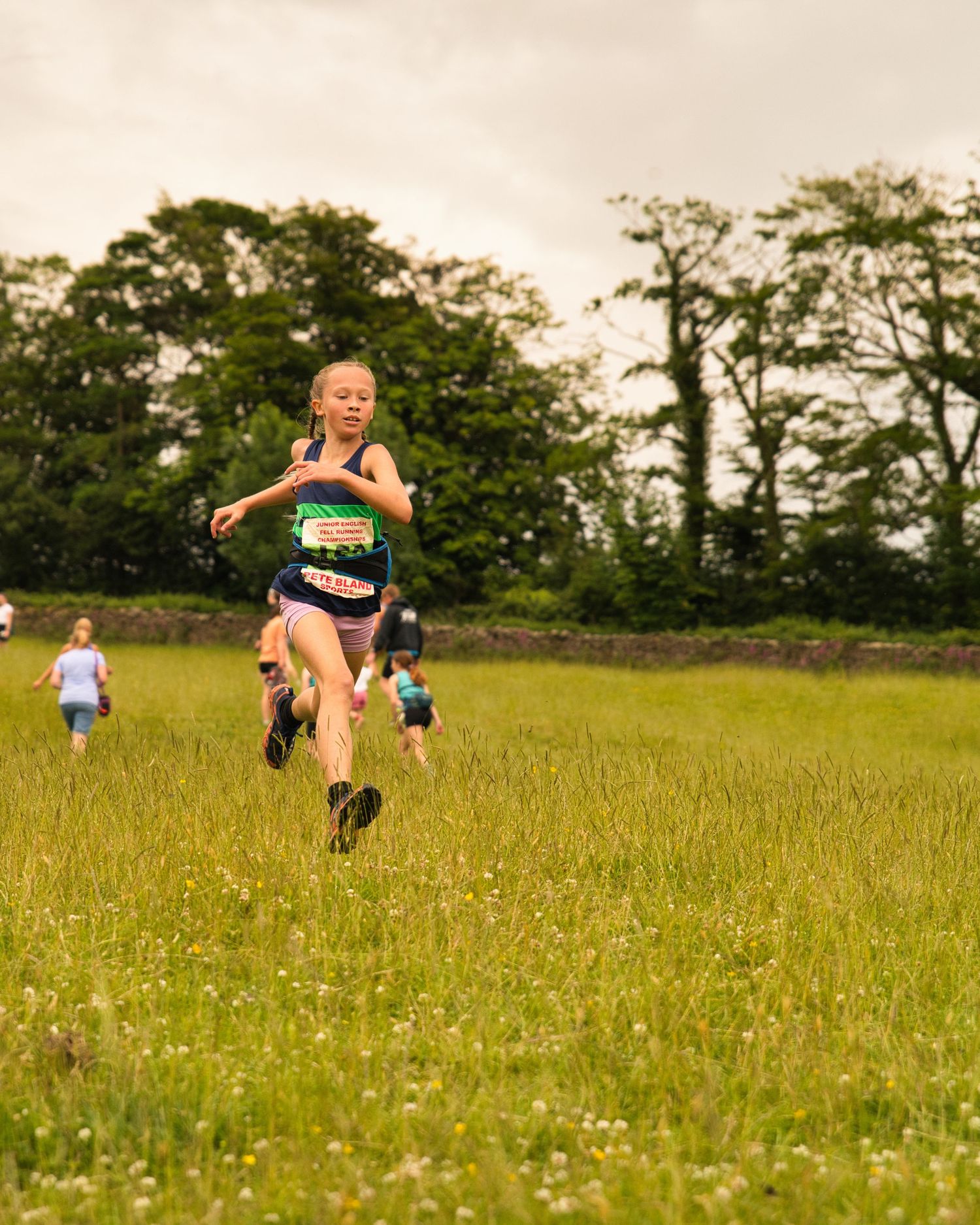 Junior fell runners descending a steep grassy hillside during a race, focused and moving fast with mountains in the background.