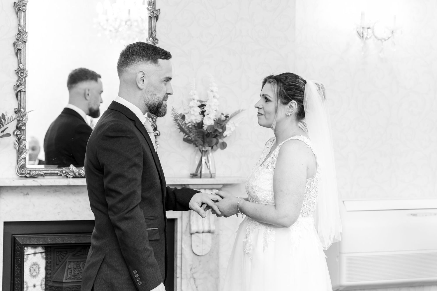 Black and white wedding photo of bride and groom holding hands at altar during ceremony.