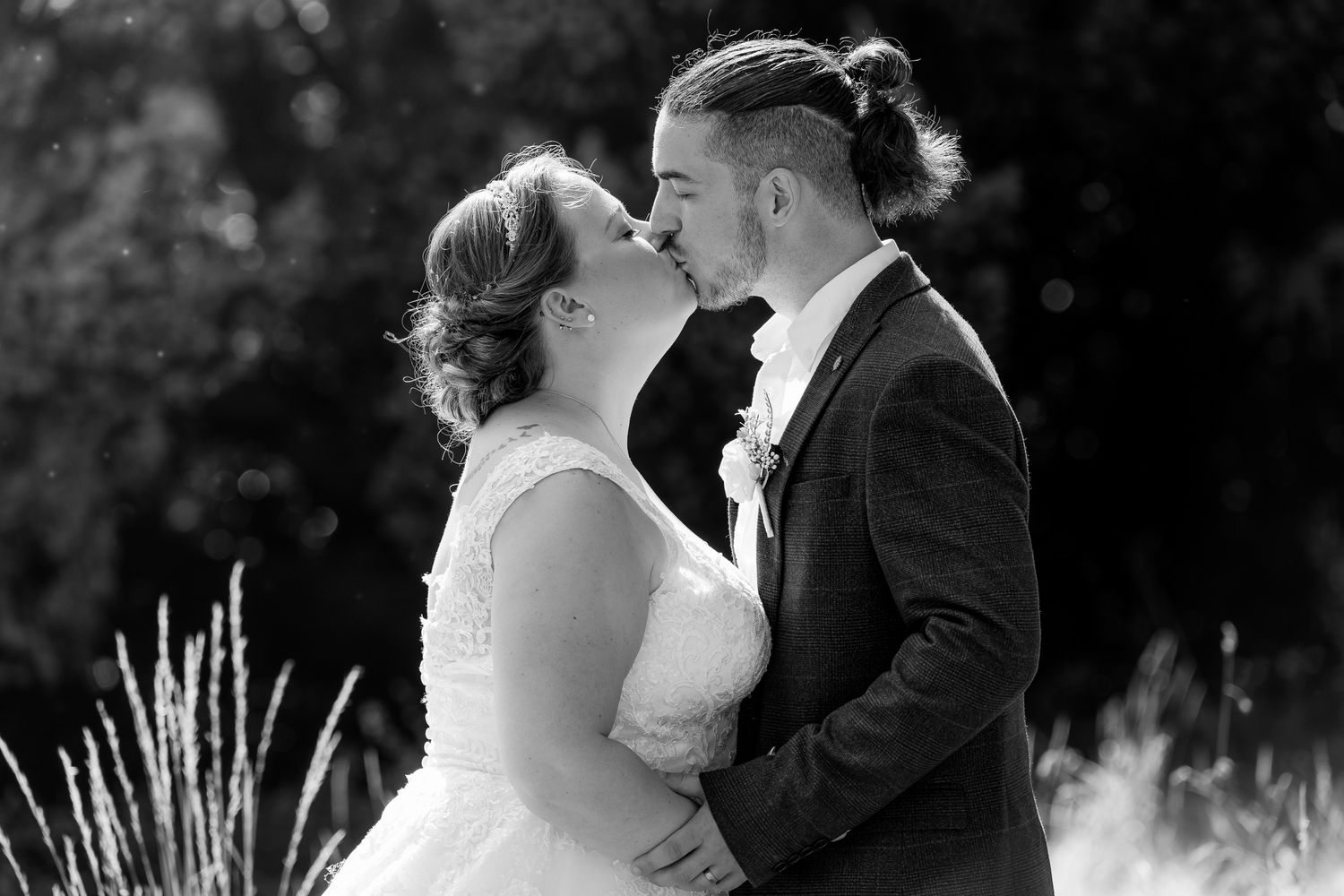 Black and white photo of bride and groom sharing romantic kiss outdoors.