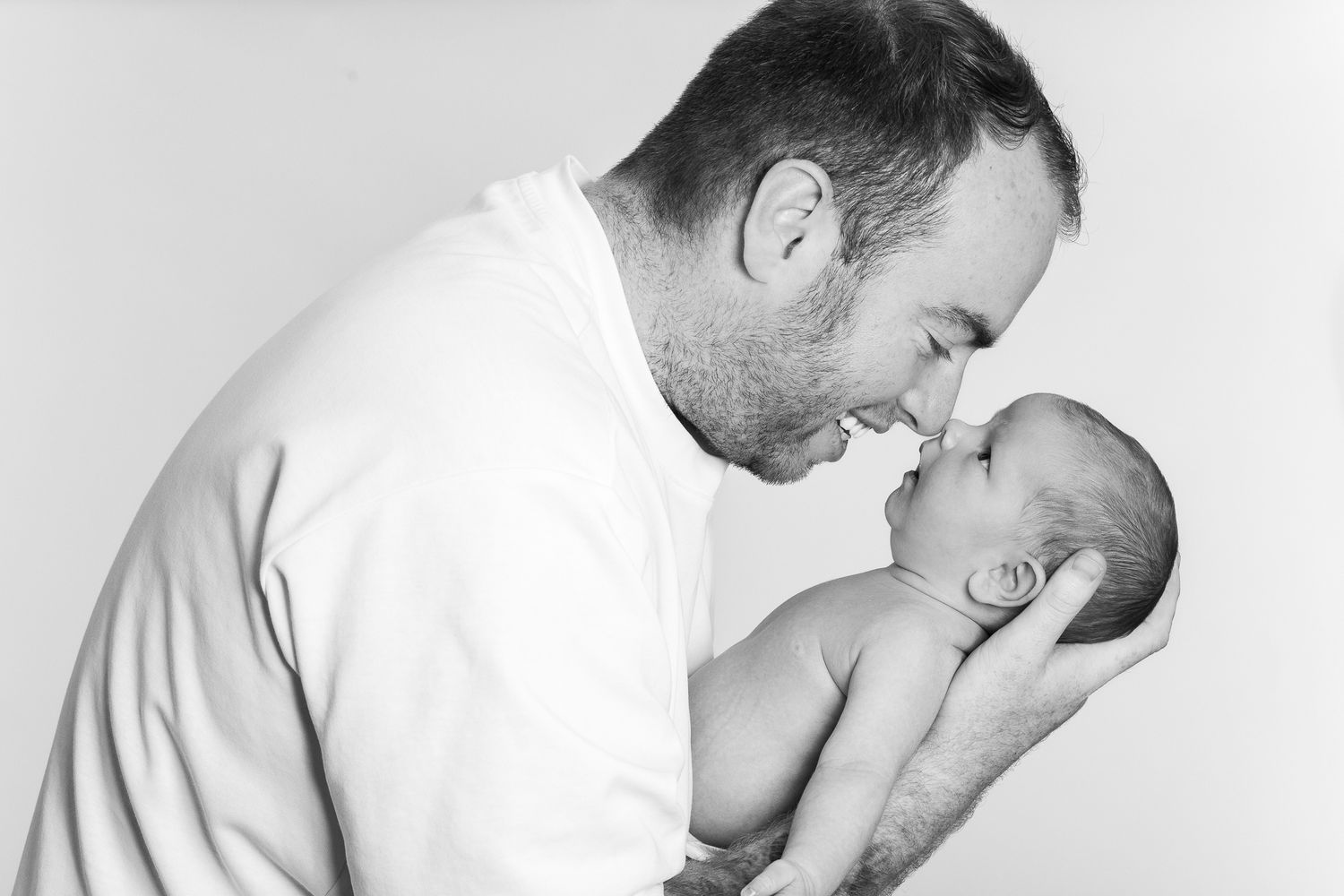Black and white portrait of a father gently touching noses with his newborn baby.