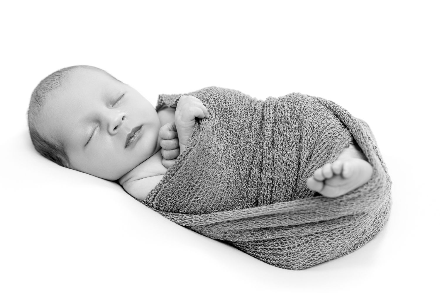 Peaceful newborn baby swaddled in a gray knit wrap in black and white.
