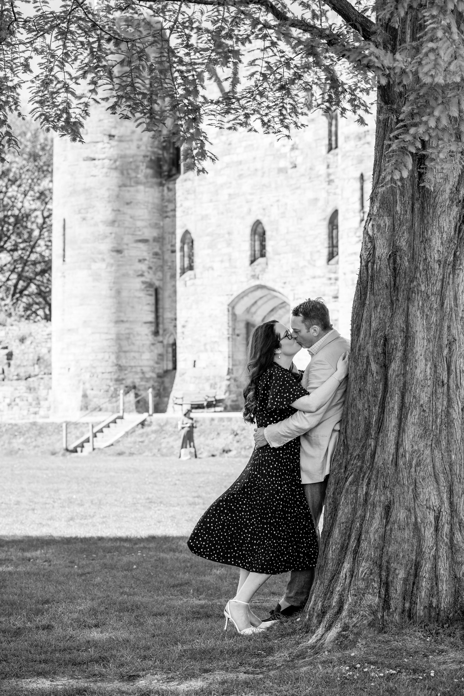 Couple embracing and kissing near a tree with a historic castle in the background.