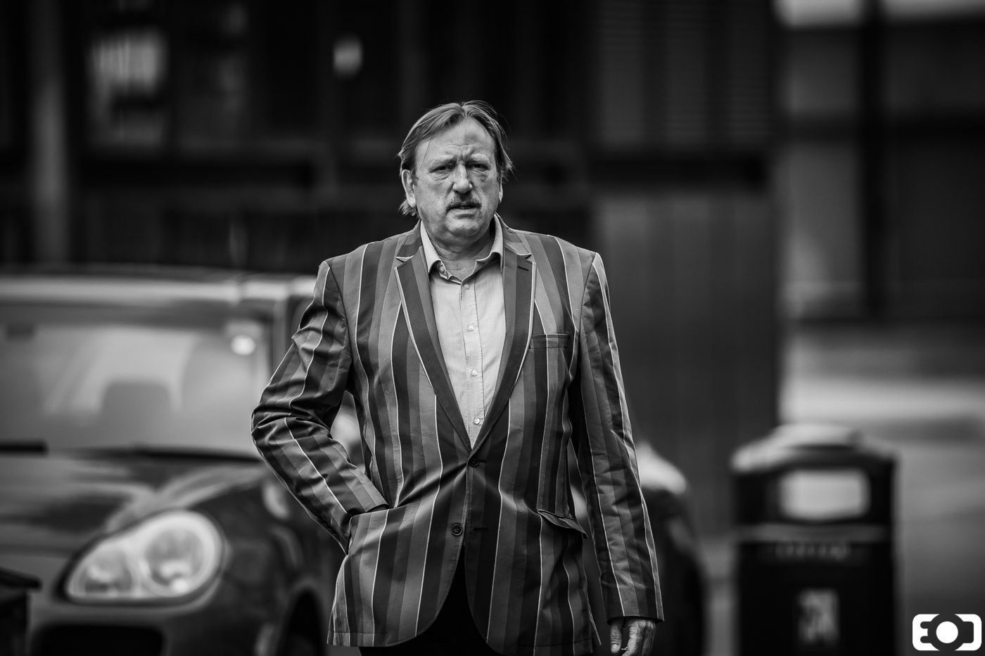Middle-aged man in striped suit walking on a city street, dramatic black and white urban portrait photography.
