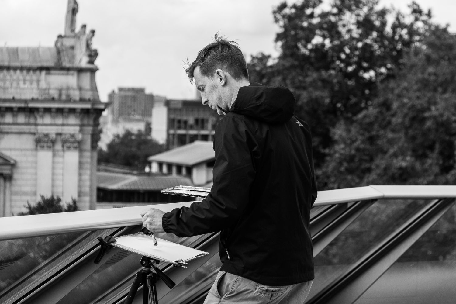 Young man in black hoodie working on equipment on a rooftop in black and white photography.