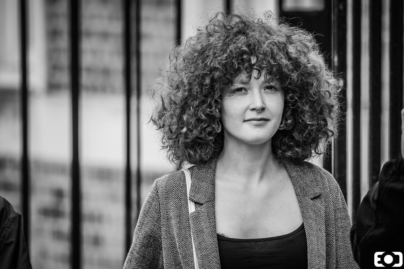 Young woman with voluminous curly hair smiling outdoors, candid black and white portrait photography.