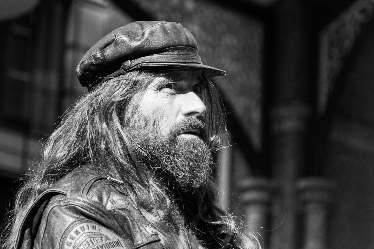 Black and white portrait of a bearded biker with long hair wearing a leather jacket.