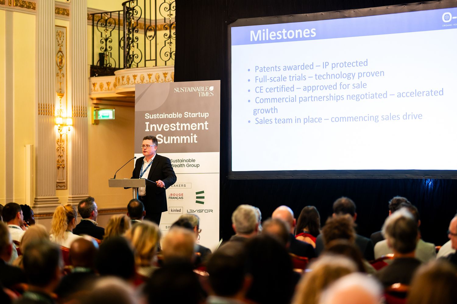 Speaker presenting milestones slide at a Sustainable Startup Investment Summit conference.