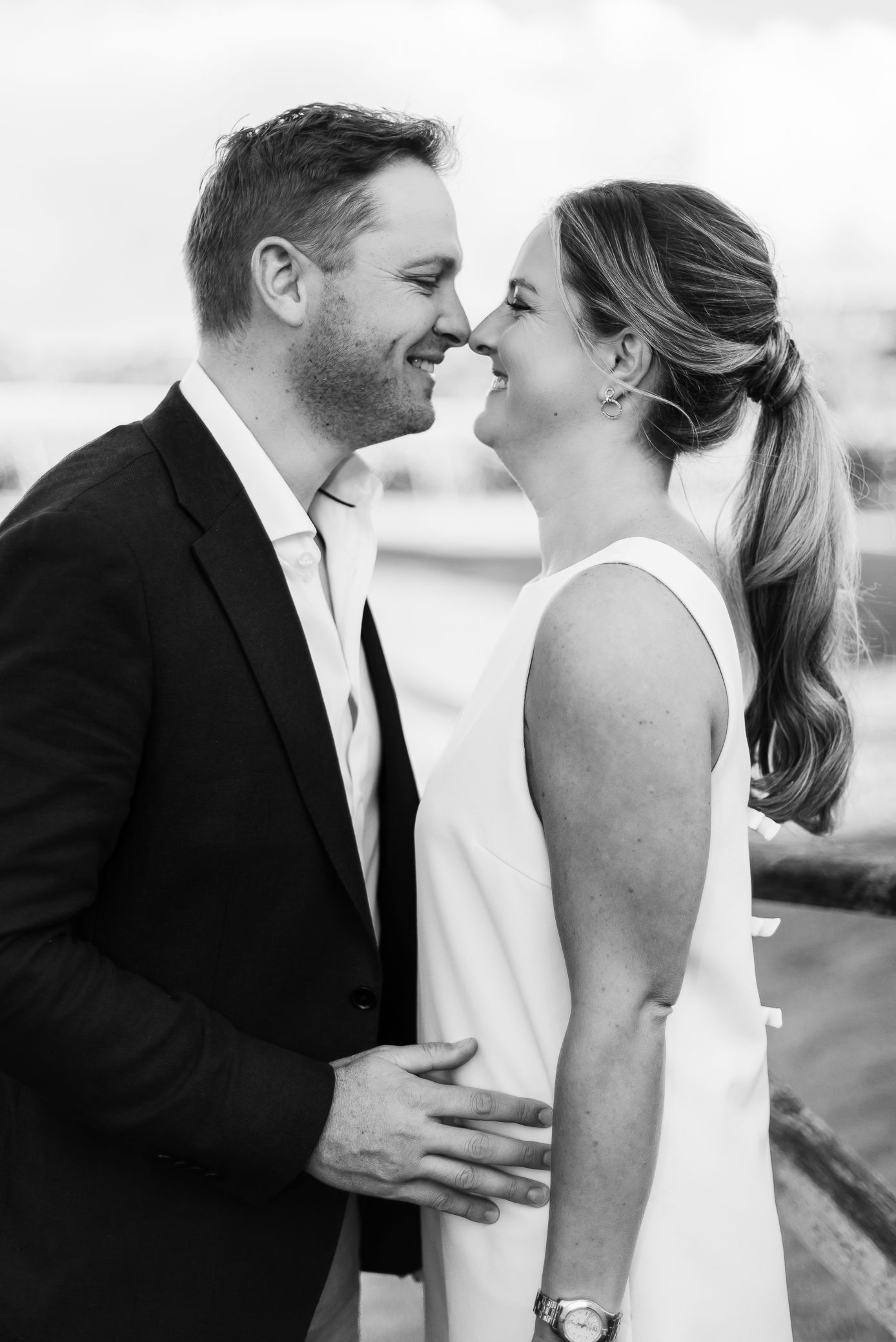 Black and white romantic portrait of smiling couple almost kissing outdoors at their engagement shoot.