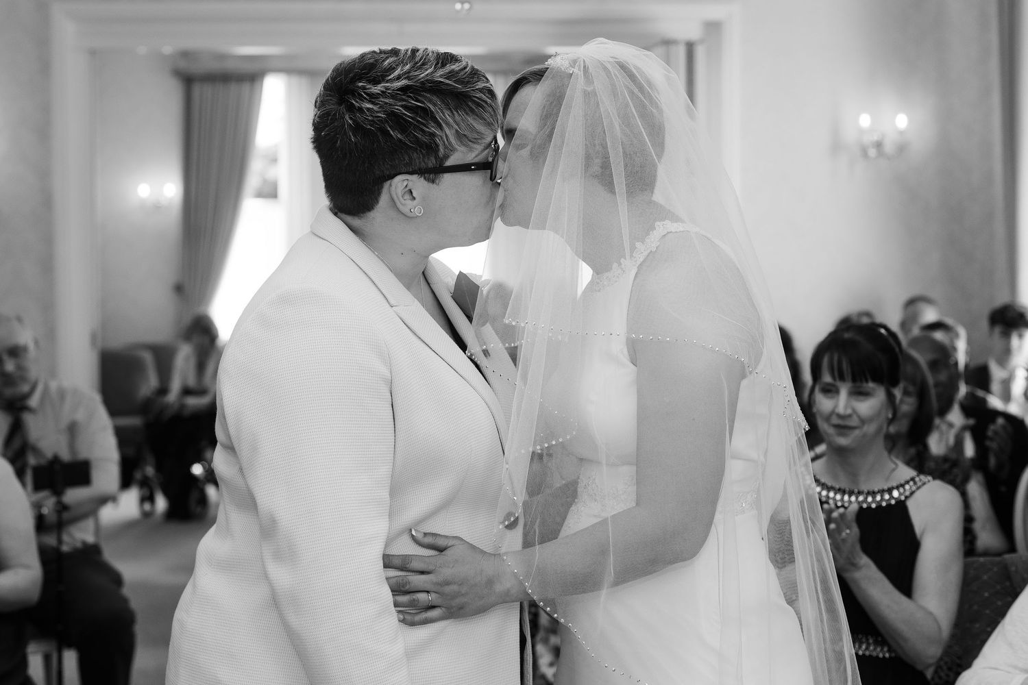 Black and white photo of two brides sharing their first kiss at the wedding ceremony altar.