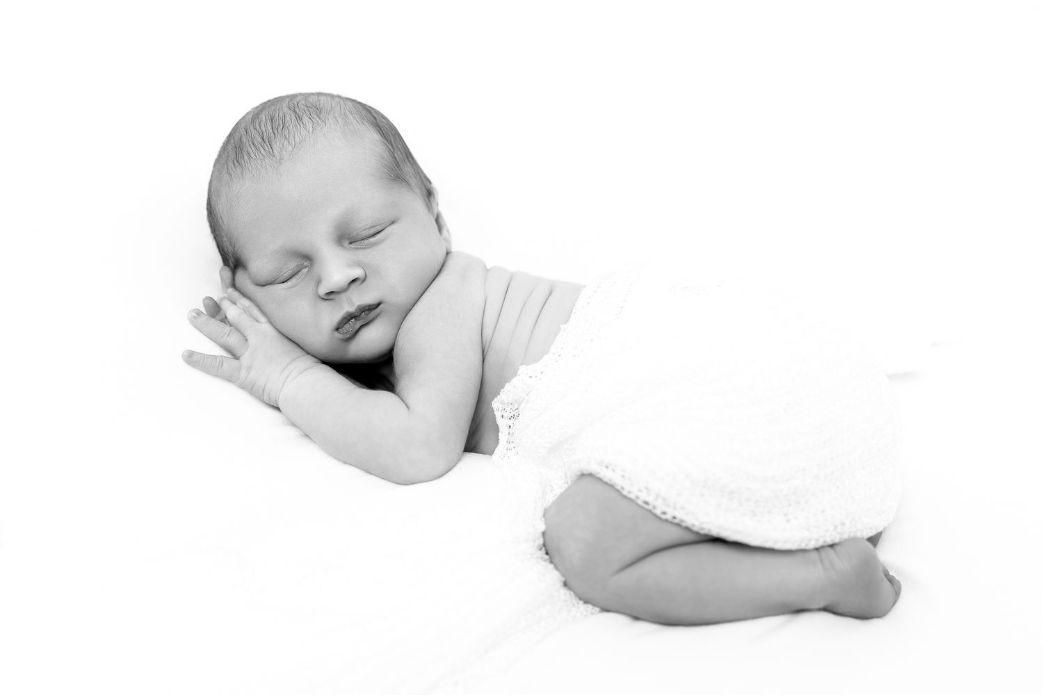 Newborn baby sleeping peacefully wrapped in a soft white blanket.