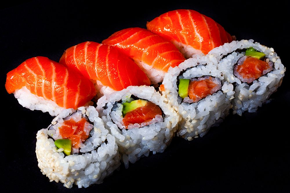 Fresh salmon nigiri and California rolls arranged on a black background.