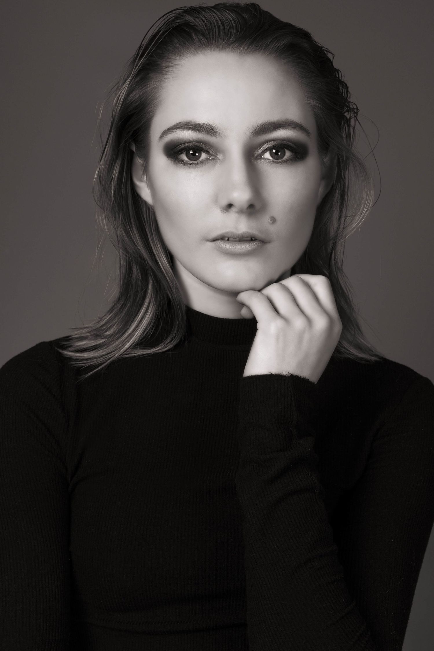 Black and white fashion portrait of a young woman in a black turtleneck resting her chin on her hand.