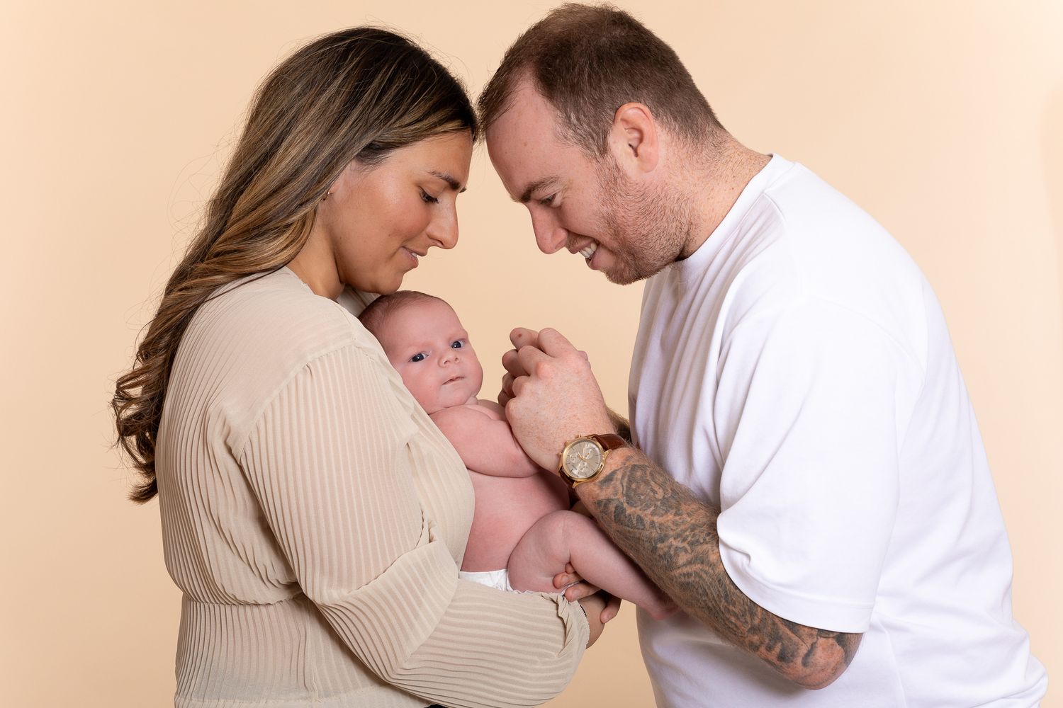 New parents lovingly holding their newborn baby together against a beige background.