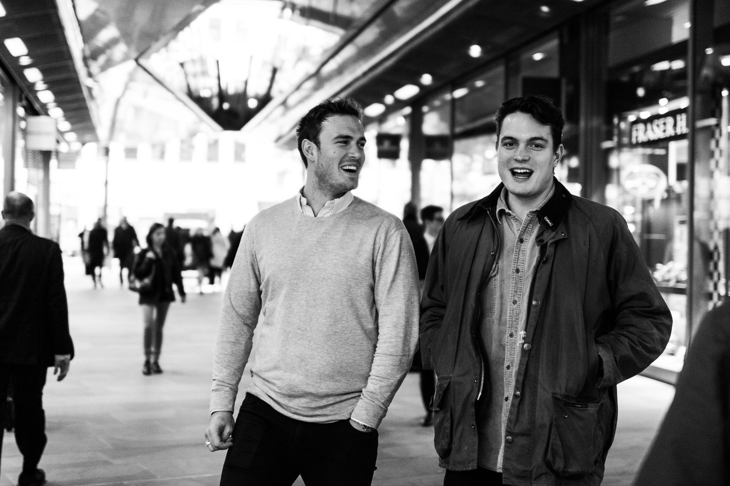 Two young men laughing together in a shopping arcade in black and white street photography.