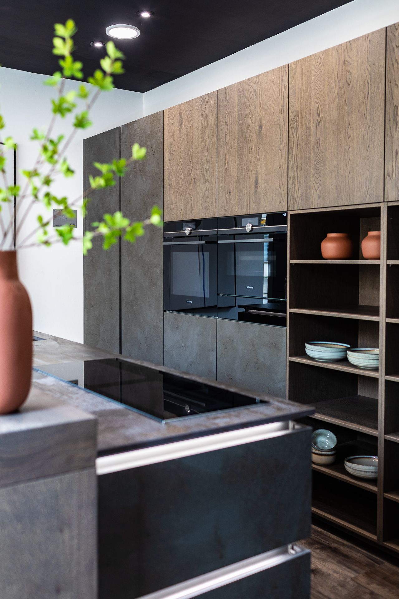 Contemporary kitchen with dark stone and wood cabinets, built-in appliances, and open shelving with ceramics.