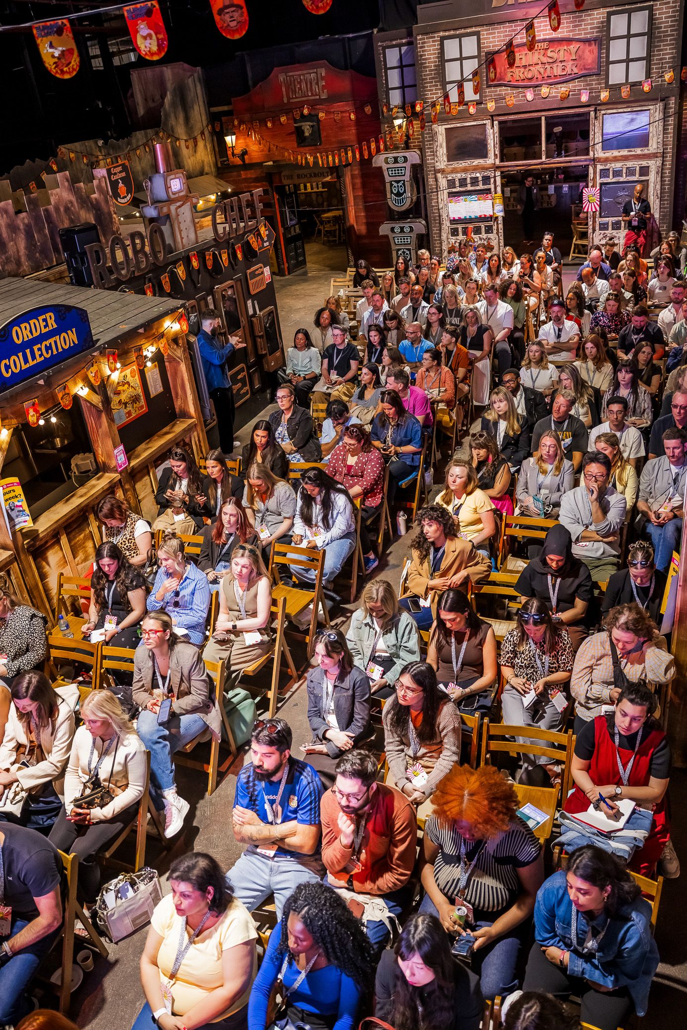Overhead view of a packed audience taking notes at an indoor conference in a decorated venue.
