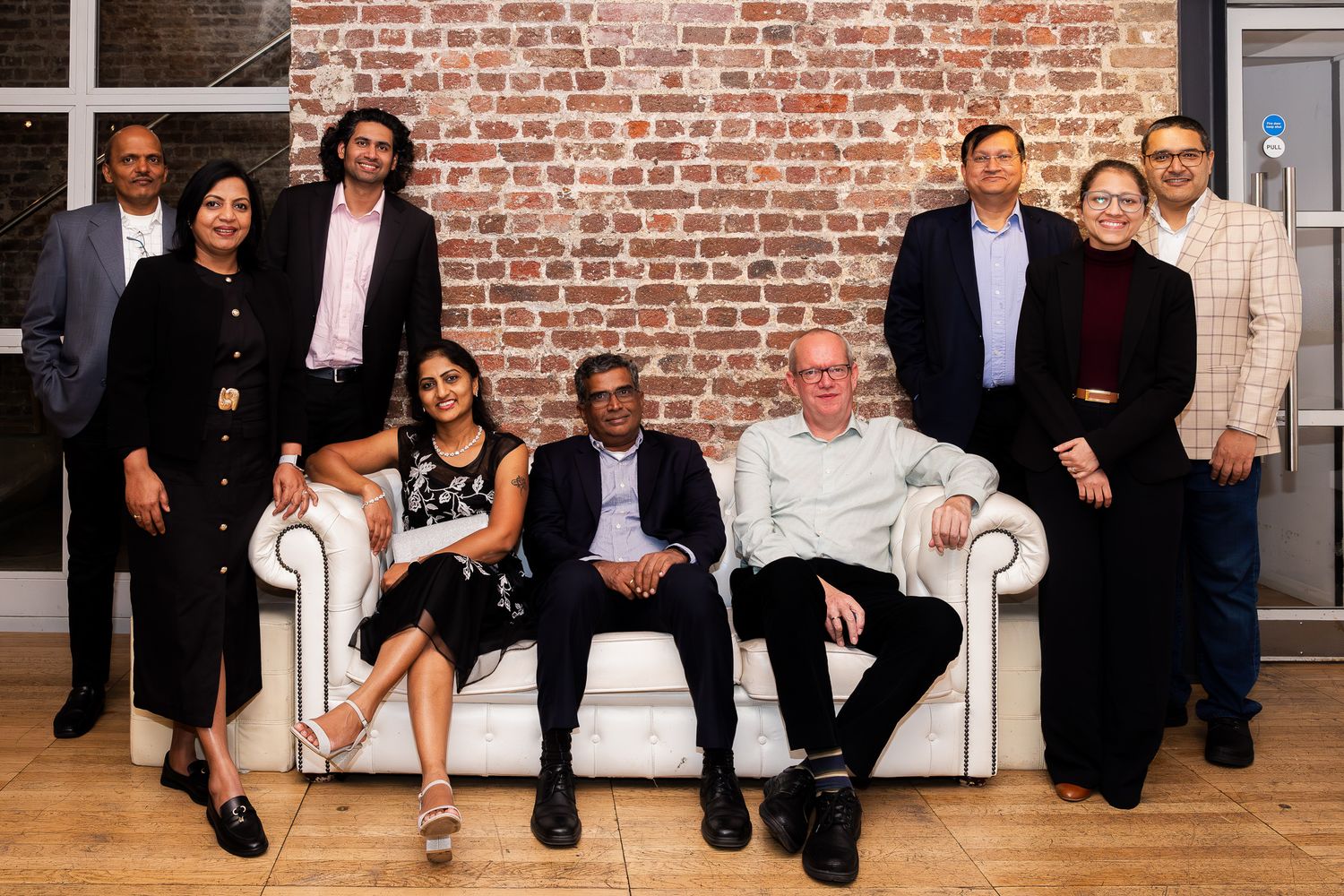 Group of ten professionals posing together in front of a brick wall at a corporate event.