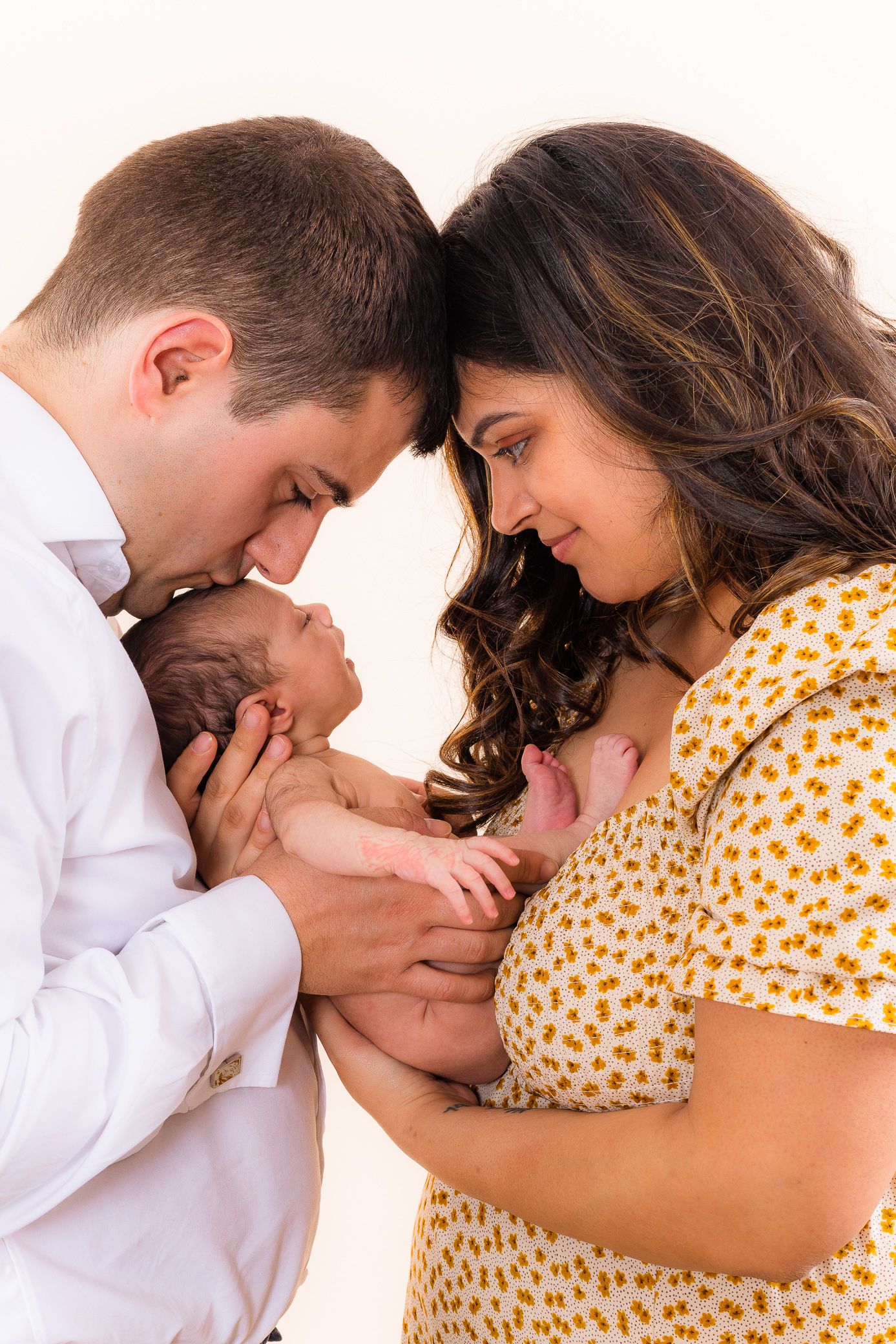 New parents lovingly cradling their newborn baby together in a warm family portrait photo.