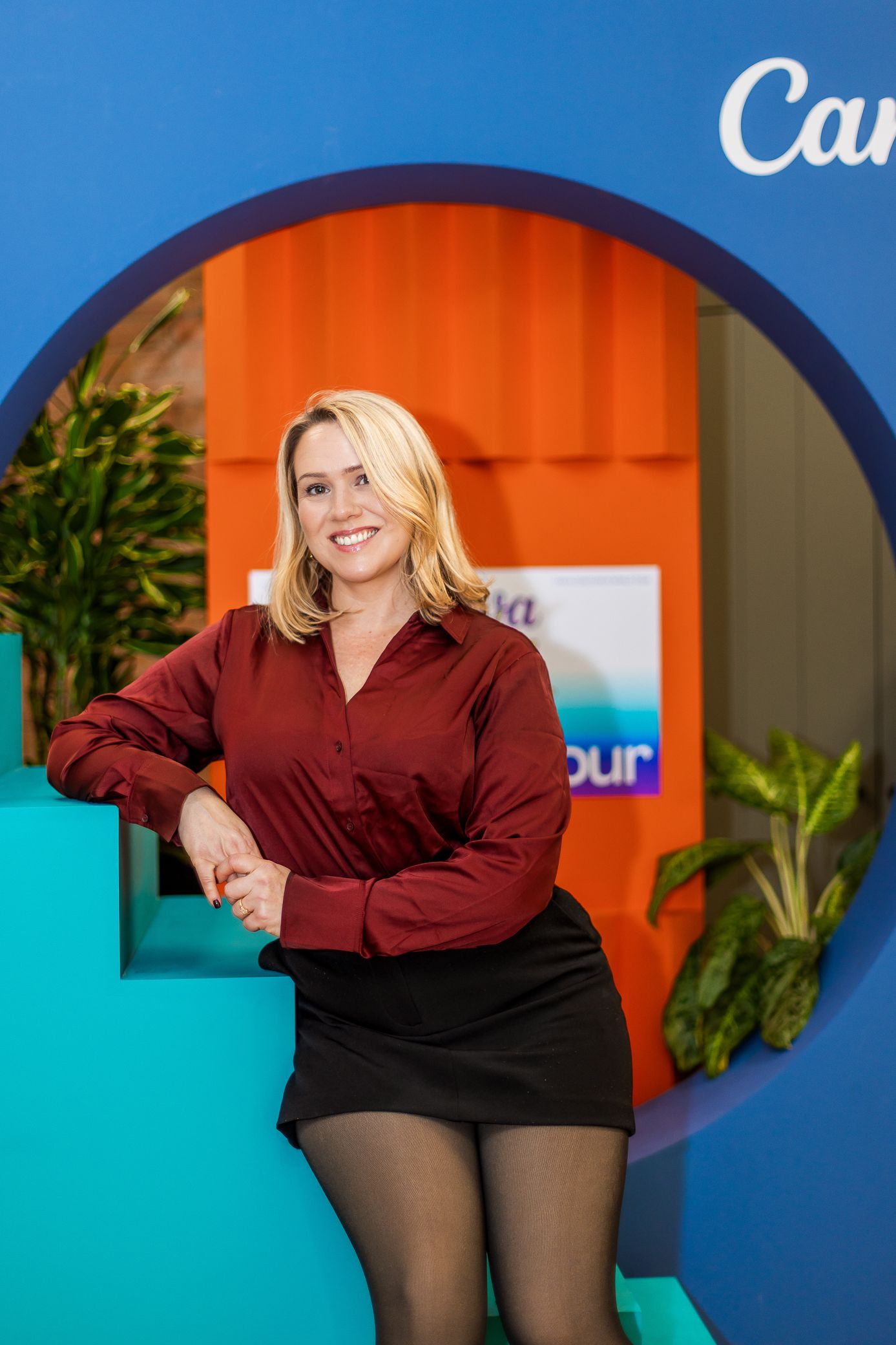 Blonde woman in burgundy shirt poses in colorful circular display at Canva event.