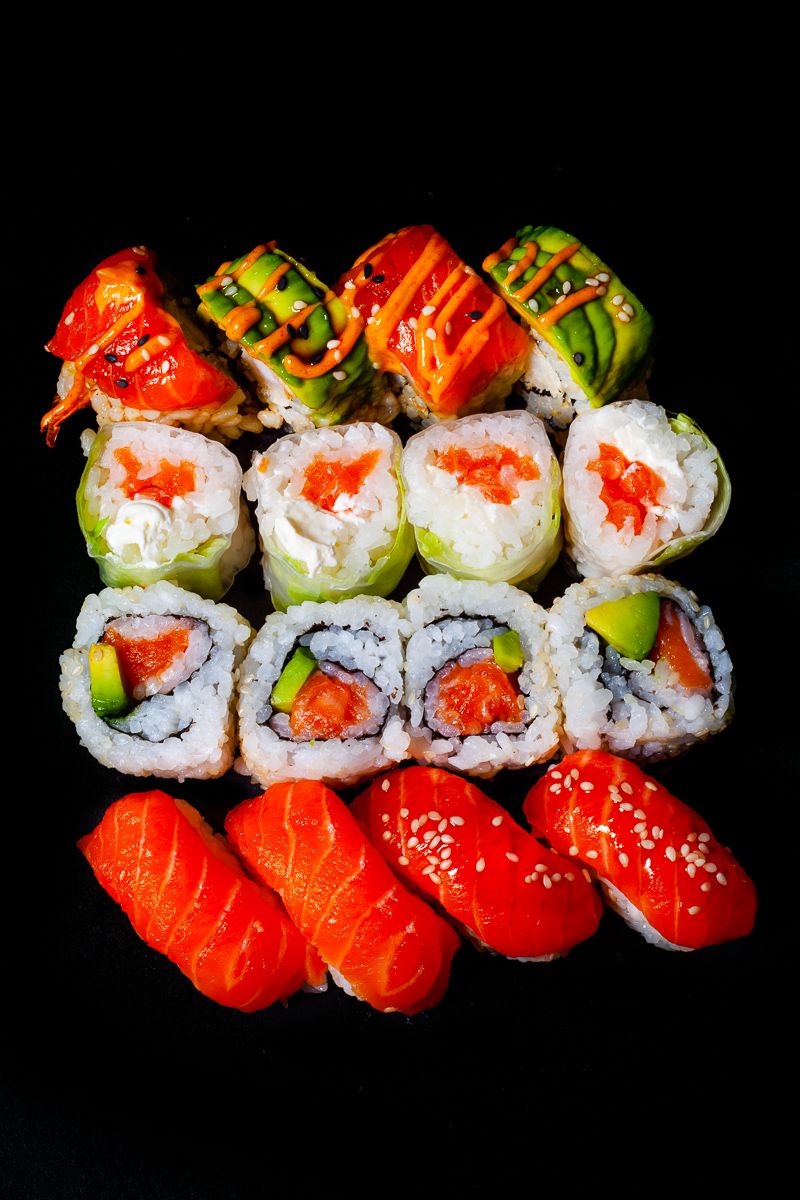 Assorted sushi platter with nigiri, California rolls, and specialty rolls on black background.