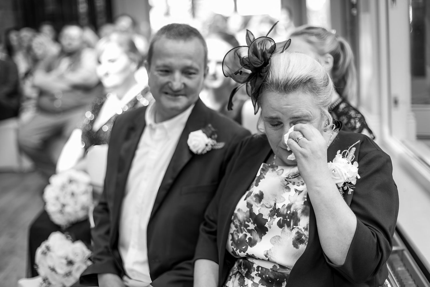 Emotional wedding guest wiping tears during ceremony, black and white candid wedding photography.