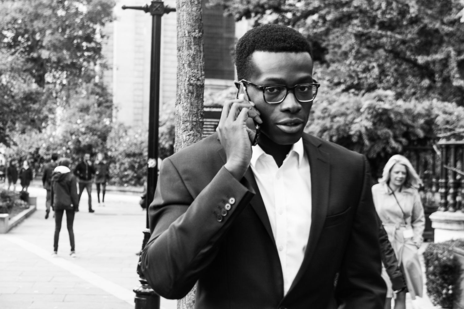 Black and white street portrait of a young man in a suit talking on his phone.