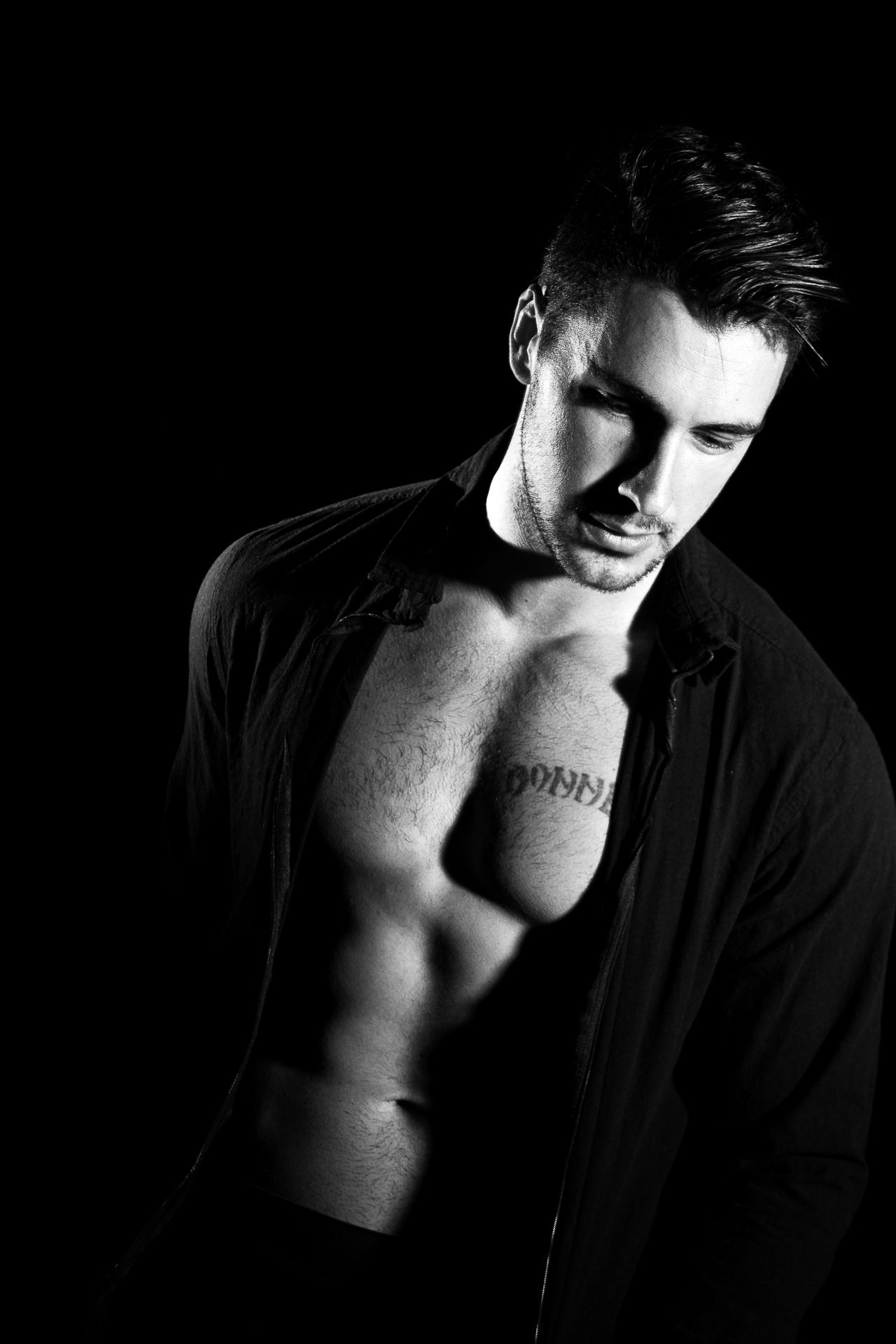 Dramatic black and white photo of a muscular tattooed man with open shirt and chiseled abs.