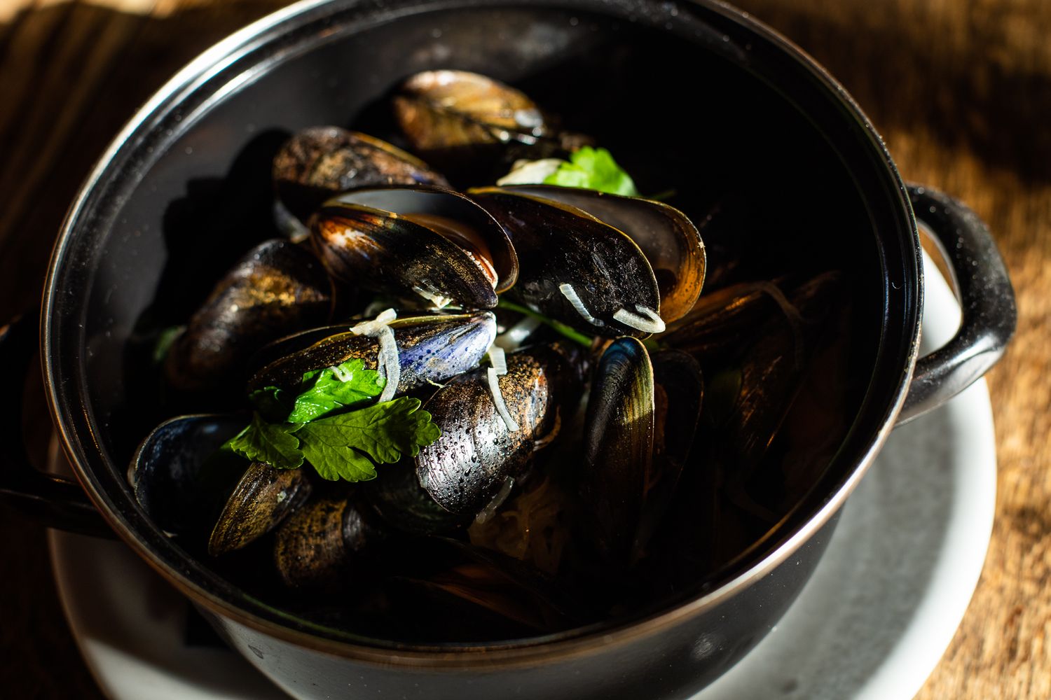 Steamed black mussels with fresh parsley garnish in classic black pot.