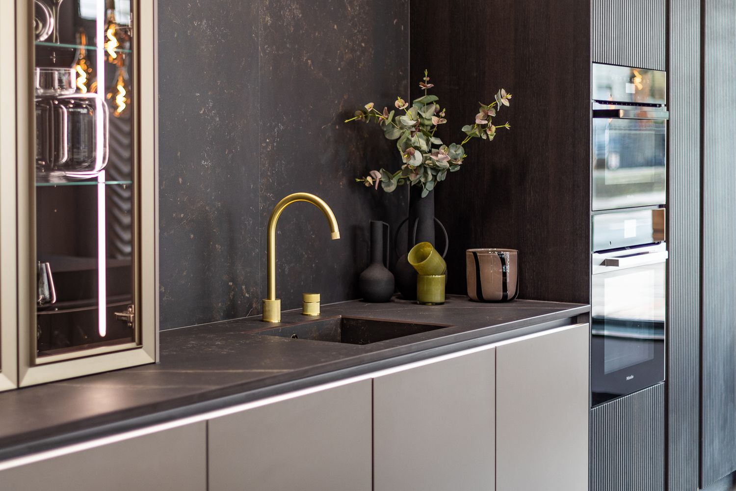 Luxury kitchen detail with gold faucet, undermount sink, dark stone countertop, and decorative black vases.