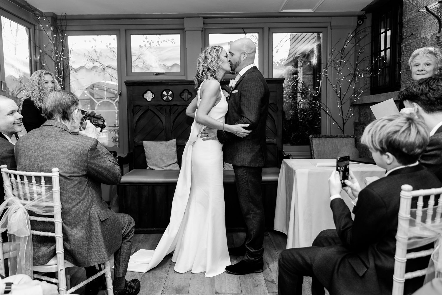Bride and groom share first kiss during intimate wedding ceremony in black and white photo.