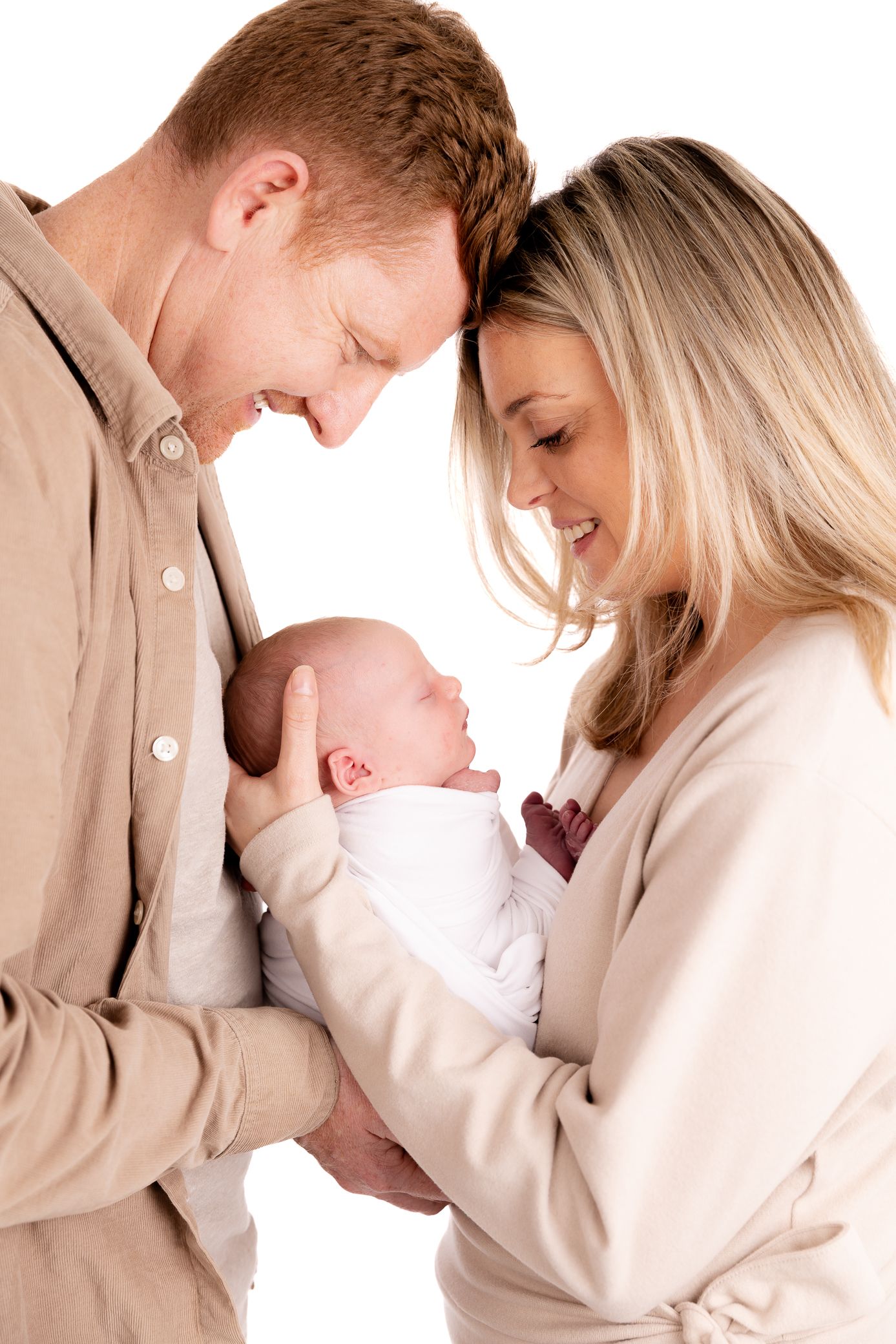 Smiling parents holding their newborn baby together against a white background.
