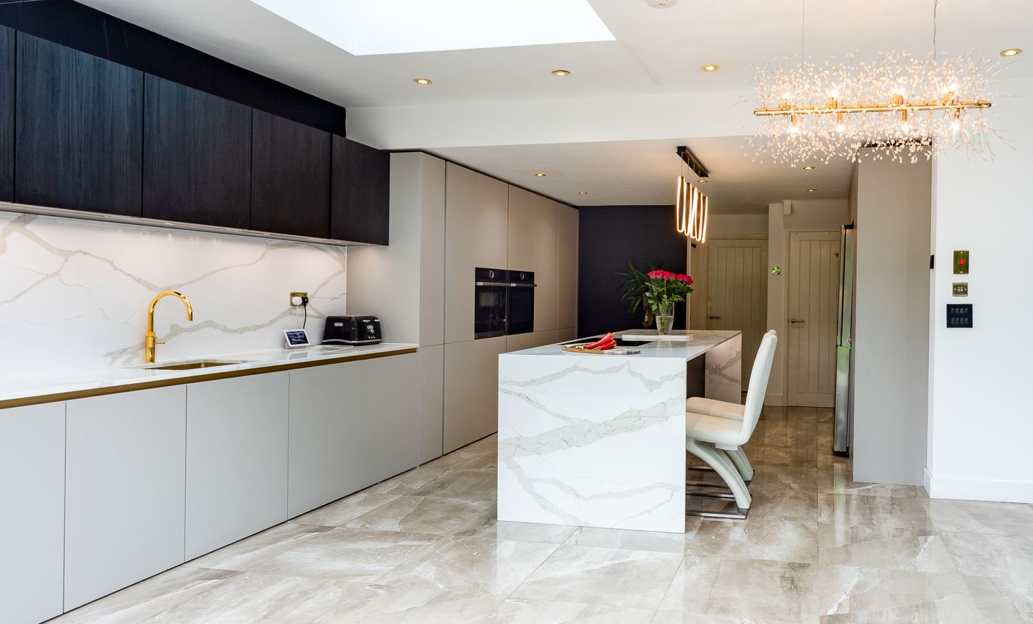 Elegant modern kitchen with marble island, grey handleless cabinets, and decorative chandelier lighting.