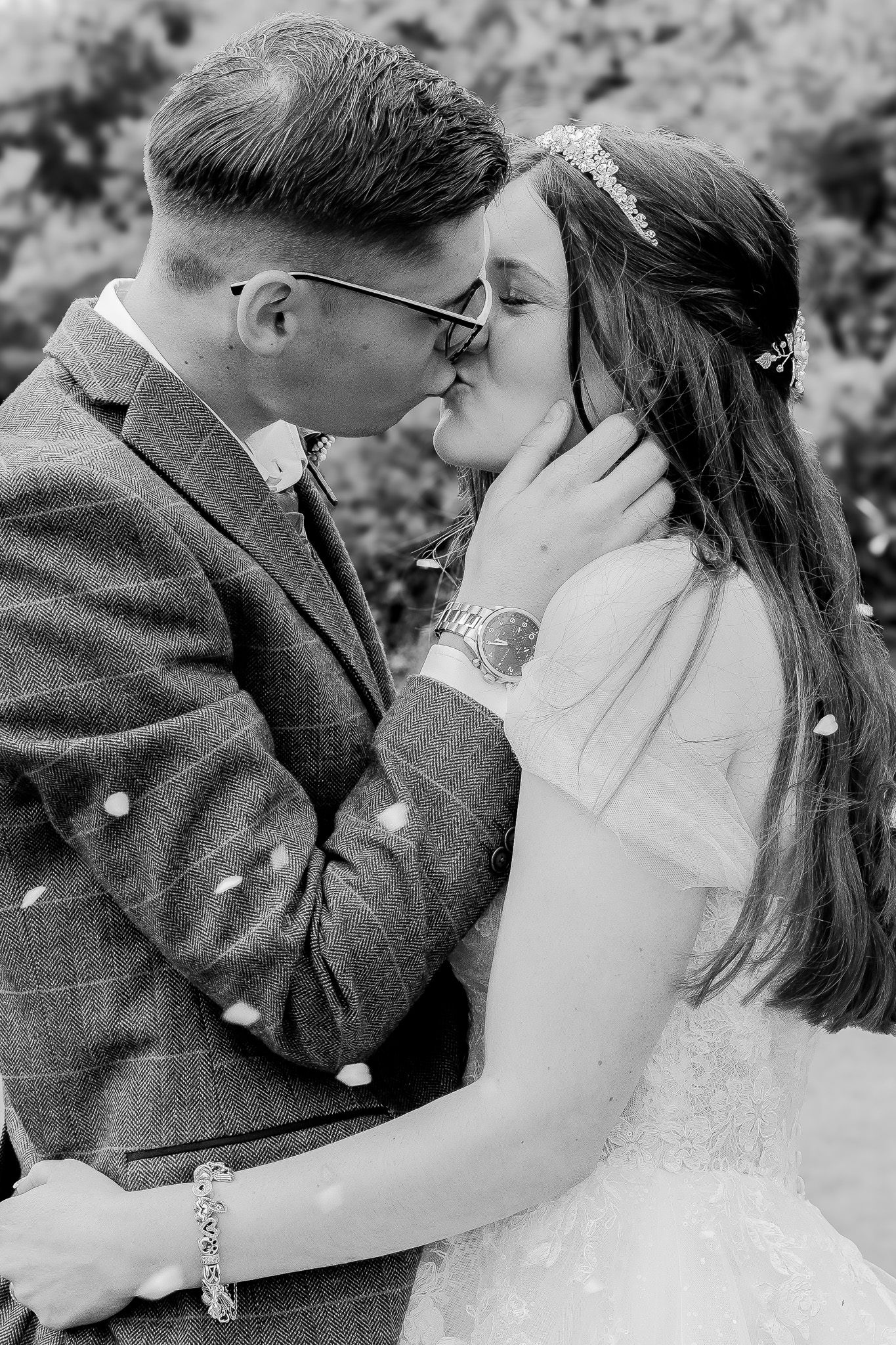 Black and white photo of a bride and groom sharing a first kiss, confetti falling around them.