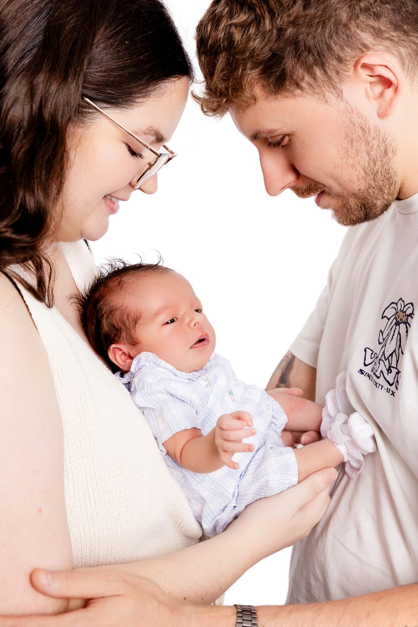 Happy young parents lovingly gazing at their alert newborn baby together.