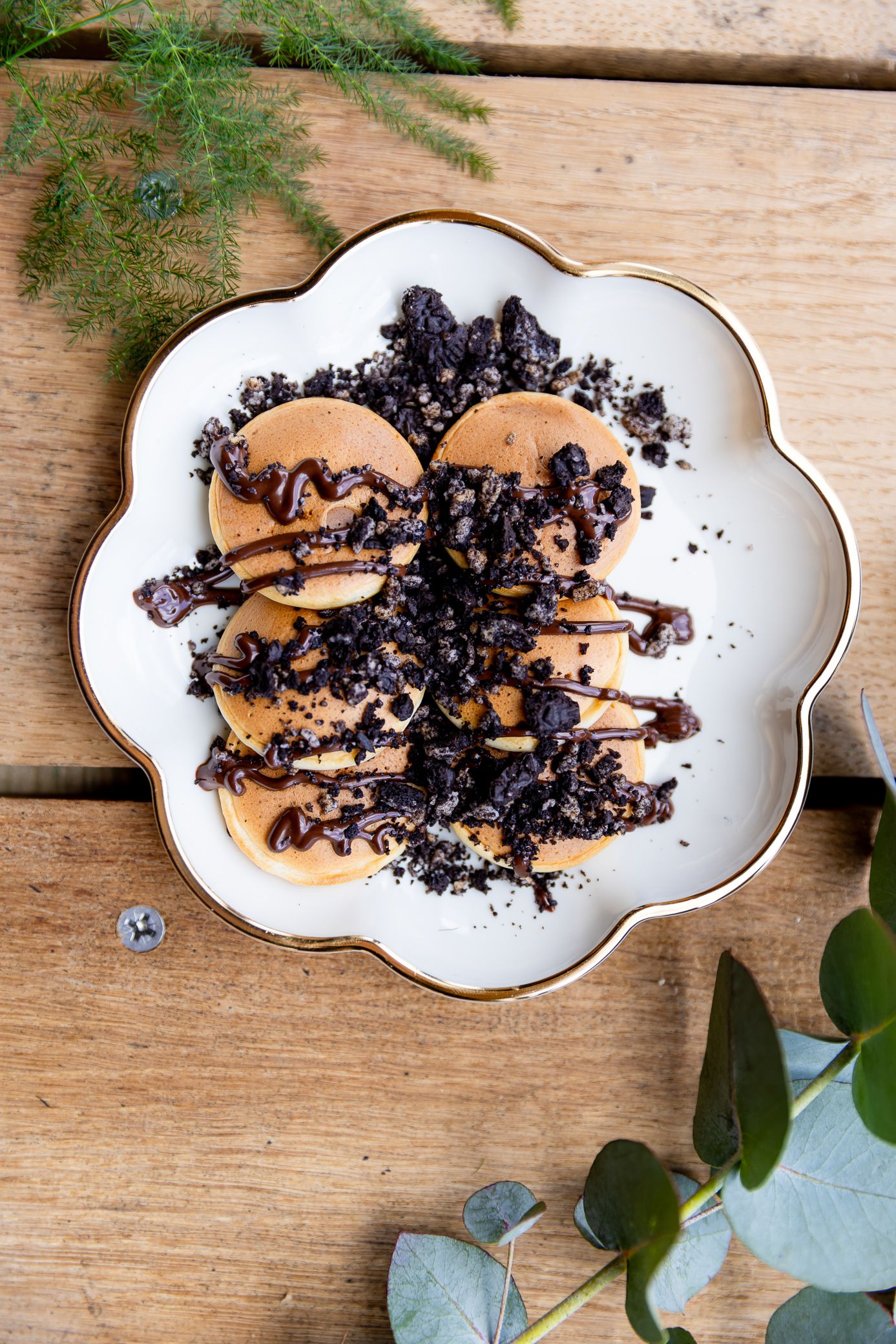 Overhead view of mini pancakes drizzled with chocolate sauce and crushed Oreo toppings on a plate.