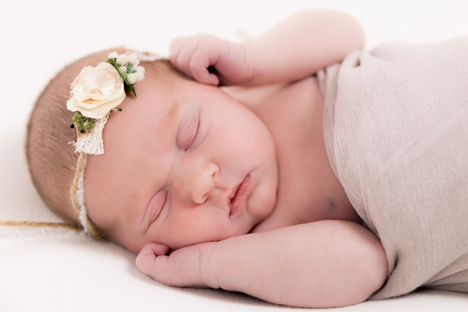 Sleeping newborn baby girl wrapped in a soft grey swaddle wearing a delicate floral headband.