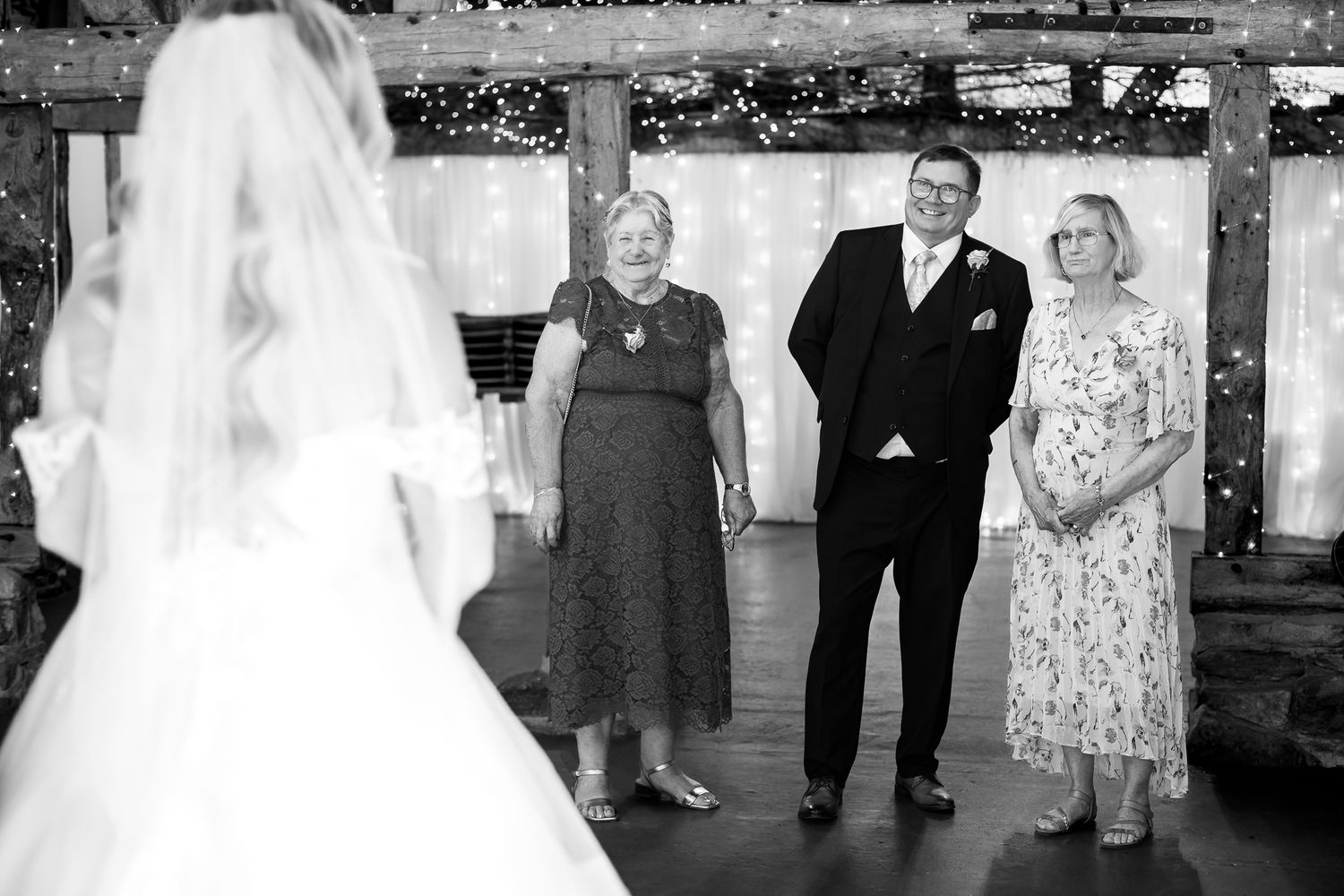 Family members smile with tears of joy as the bride approaches in a black and white ceremony photo.