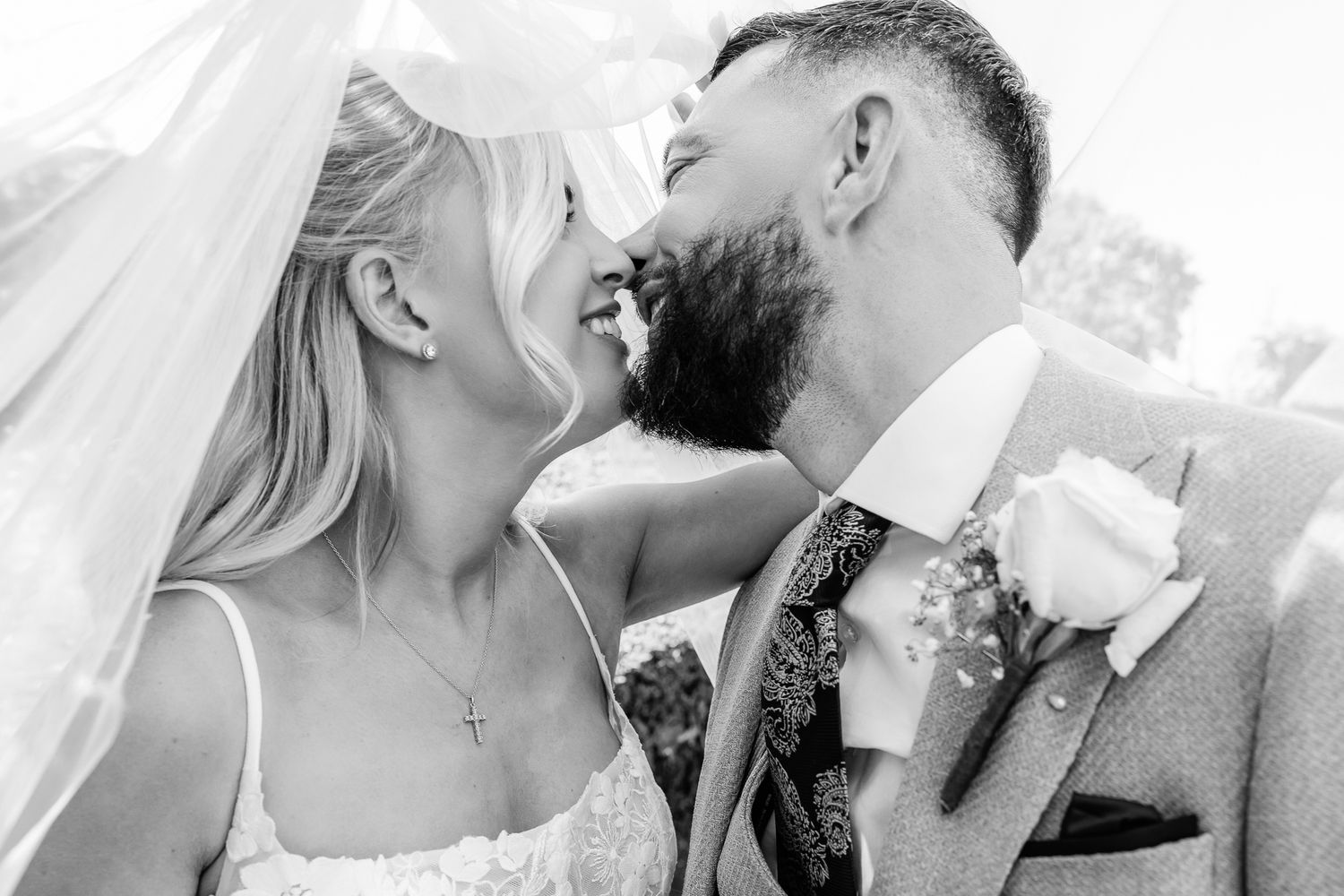 Black and white photo of a bride and groom laughing together under a veil on their wedding day.