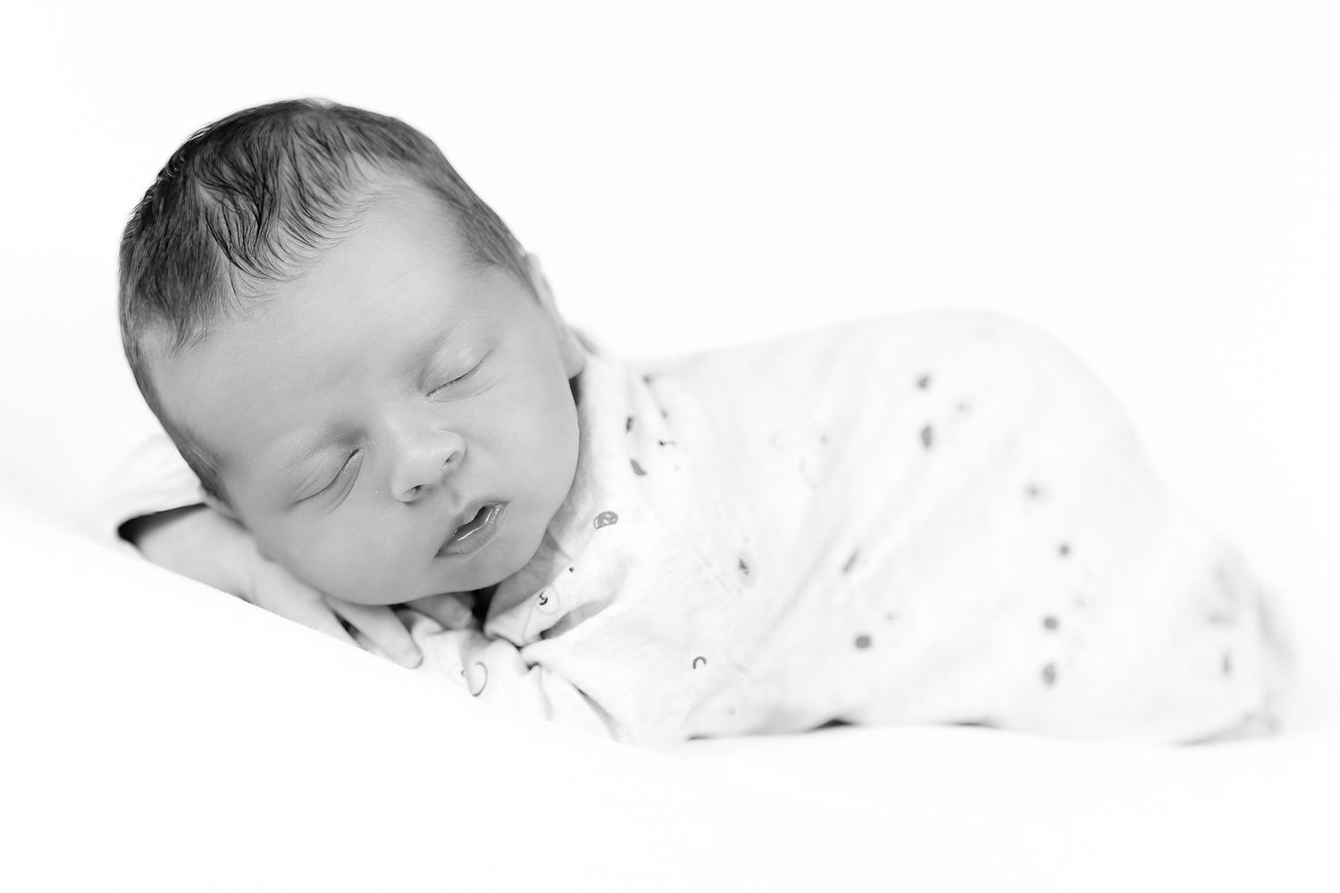 Black and white portrait of a sleeping newborn baby wrapped in a white swaddle.