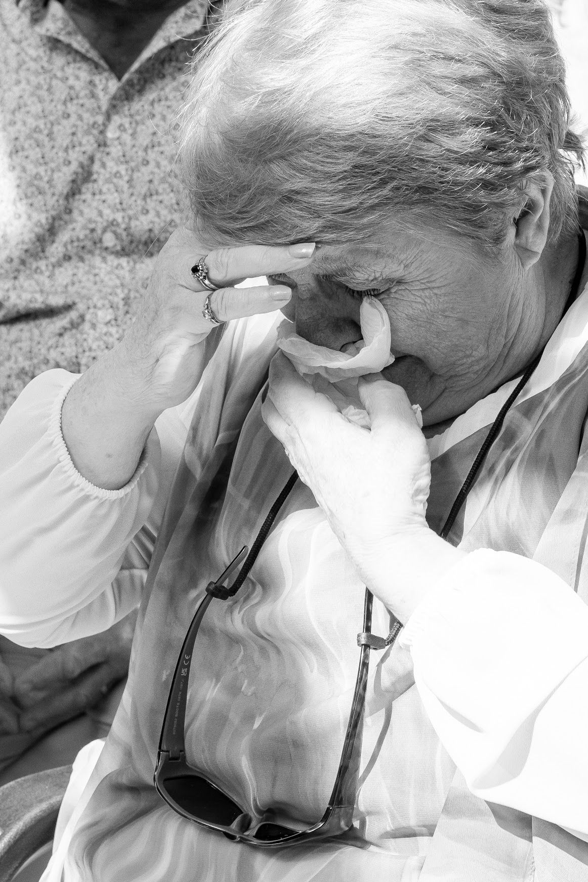 Elderly woman wiping tears with handkerchief, emotional black and white candid wedding moment.
